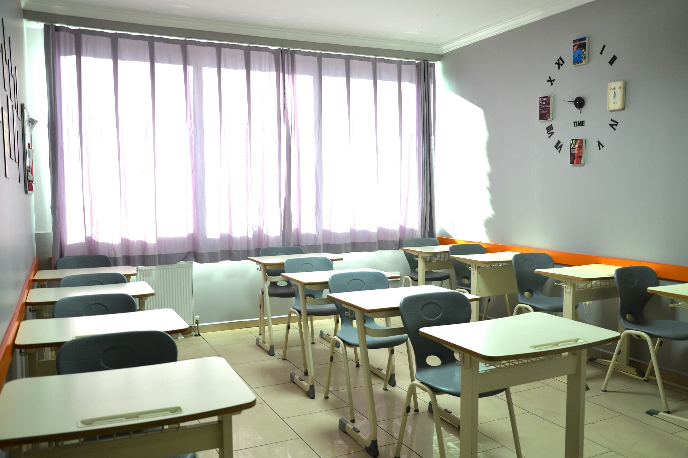 Boş bir derslik: tek kişilik sıralar, geniş pencere ve duvar saati.